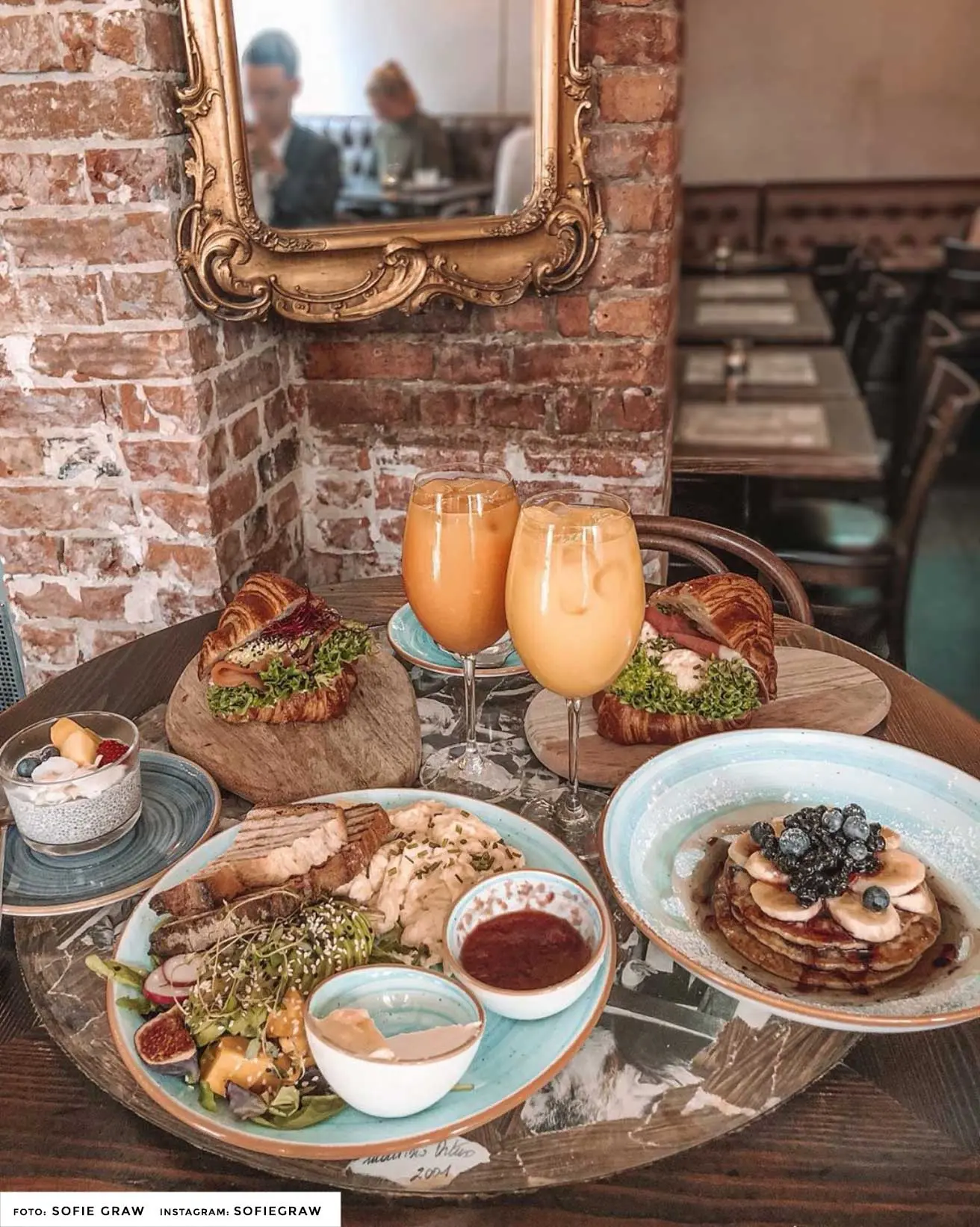 Café Fix brunch med croissanter, pannkakor och juice på ett träbord framför tegelvägg